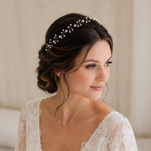 Charger l'image dans la galerie, Bandeau de perles de mariée porté sur chignon brun, vue de trois quarts dans une ambiance de mariage lumineuse
