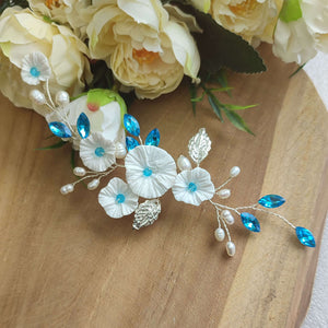 Vigne de cheveux avec fleurs blanches, feuilles argentées, perles naturelles et cristaux de strass bleu pour chignon de mariage