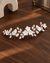 Charger l'image dans la galerie, Bijou de cheveux argenté à fleurs et boutons en porcelaine blanche sur fil or rose présenté à plat sur fond noyer foncé