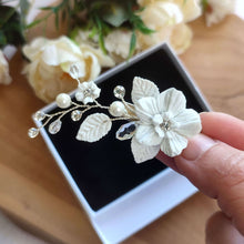 Charger l&#39;image dans la galerie, Détail du bijou de cheveux Audra tenu en main, fleurs en porcelaine blanche et strass étincelants