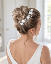 Charger l'image dans la galerie, Mariée blonde vue de dos avec un chignon haut travaillé, agrémenté d’une vigne de fleurs blanches, perles et cristaux sur fil argenté.