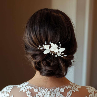 Bijou de cheveux Aliénor porté sur un chignon bas de mariée, décoré de fleurs et feuilles en porcelaine blanche avec perles et strass transparents