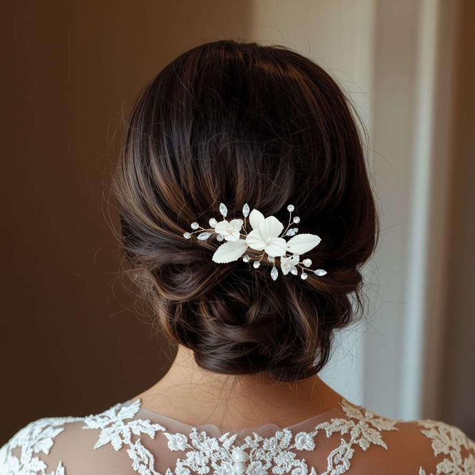 Bijou de cheveux Aliénor porté sur un chignon bas de mariée, décoré de fleurs et feuilles en porcelaine blanche avec perles et strass transparents