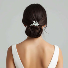 Charger l&#39;image dans la galerie, Bijou de cheveux Daria en porcelaine blanche porté sur un chignon bas de mariée, accessoire floral délicat.