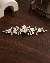Charger l'image dans la galerie, Bijou de cheveux argenté à fleurs et boutons en porcelaine blanche sur fil doré présenté à plat sur fond noyer foncé
