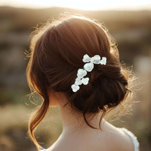 Charger l&#39;image dans la galerie, Bijou de cheveux SIANA, fleurs en porcelaine blanche sur chignon bas flou dans une lumière dorée, accessoire poétique pour mariée.