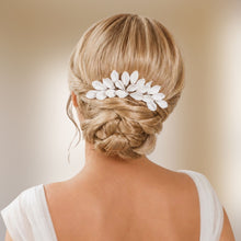 Charger l'image dans la galerie, Peigne de mariée aux feuilles blanches en porcelaine froide porté horizontalement au-dessus d’un chignon bas blond tressé.
