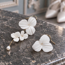 Charger l'image dans la galerie, Paire de boucles d’oreilles asymétriques posée sur une pierre grise, composée de fleurs blanches en porcelaine froide et de perles naturelles