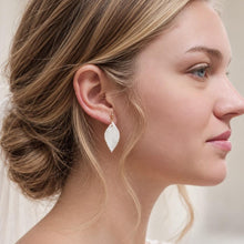 Charger l'image dans la galerie, Mariée, vue de profil, portant des boucles d’oreilles pendantes feuilles blanches en porcelaine, avec chignon bas et robe de mariée en dentelle