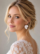 Charger l'image dans la galerie, Boucle d’oreille de mariage composée de trois petites fleurs blanches en porcelaine et de perles nacrées, portée avec une coiffure relevée.