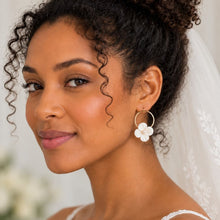 Charger l'image dans la galerie, Boucles d'oreilles de mariée avec fleurs blanches en porcelaine froide et cercles dorés, portées avec un chignon haut bouclé.