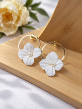 Charger l'image dans la galerie, Boucles d'oreilles de mariage avec fleurs blanches nervurées en porcelaine froide, perles et cercles dorés, présentées sur un support en bois clair.