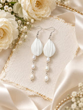 Charger l'image dans la galerie, Boucles d'oreilles pendantes artisanales avec feuilles en porcelaine froide et trois perles d'eau douce, finitions argentées, sur fond romantique ivoire.