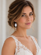 Charger l'image dans la galerie, Mariée coiffée d'un chignon flou portant une boucle d'oreille longue avec feuille blanche sculptée et perles naturelles, robe de mariée en dentelle.