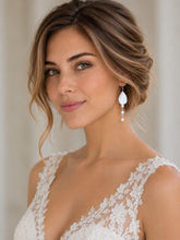 Charger l'image dans la galerie, Mariée portant une longue boucle d'oreille en porcelaine blanche et perles d'eau douce, avec une coiffure relevée et une robe en dentelle.