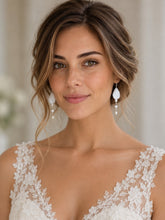 Charger l'image dans la galerie, Mariée vue de face avec chignon romantique et paire de boucles d'oreilles pendantes en porcelaine blanche et perles naturelles, robe en dentelle florale.