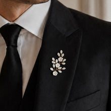Charger l'image dans la galerie, Marié en costume noir portant la boutonnière Tamara avec fleurs blanches et détails dorés, accessoire mariage élégant et minimaliste.