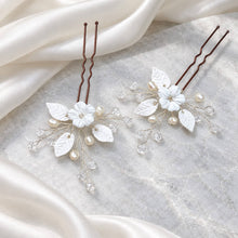 Charger l'image dans la galerie, Deux épingles de mariage avec fleurs et feuilles blanches en porcelaine froide, perles naturelles et cristaux transparents, sur fil argenté, photographiées à plat sur fond marbré