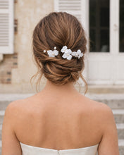 Charger l'image dans la galerie, Épingles à cheveux avec fleurs en porcelaine blanche et perles naturelles, placées sur un chignon bas de mariée, vue de dos.