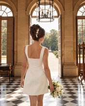 Charger l'image dans la galerie, Mariée vue de dos dans une robe blanche, coiffée d’un chignon haut orné d’épingles florales.