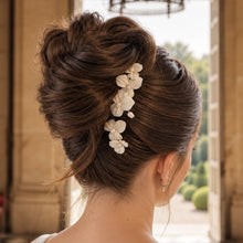 Charger l'image dans la galerie, Épingles à fleurs en porcelaine blanche disposées dans un chignon haut de mariée, vue de trois quarts.