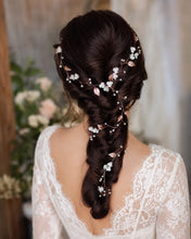 Charger l'image dans la galerie, Une longue vigne de cheveux flexible ornée de feuilles métalliques en or rose, de petites fleurs blanches et de minuscules perles transparentes. L'accessoire est mis comme couronne, puis tressé dans une coiffure brune, descendant jusqu'au bas de la tresse.