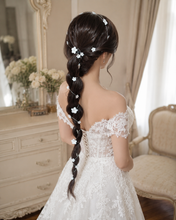 Charger l'image dans la galerie, Mariée en robe de dentelle portant une longue vigne de fleurs blanches enroulée autour d’une tresse brune jusqu’au fessier.