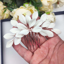 Charger l'image dans la galerie, Peigne floral avec feuilles en porcelaine blanche pour coiffure de mariée, finition or rose, photographié dans une main
