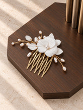 Charger l'image dans la galerie, Peigne cheveux mariage blanc en porcelaine et perles, finition dorée, posé à plat sur un socle en bois foncé.