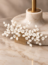 Charger l'image dans la galerie, Peigne cheveux mariage avec fleurs et feuilles en porcelaine blanche sur fil doré, appuyé sur socle en marbre beige