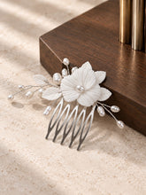 Charger l'image dans la galerie, Peigne floral mariage en porcelaine blanche et perles naturelles, présenté en finition argenté devant un socle en bois foncé.