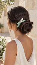 Charger l'image dans la galerie, Mariée de profil portant un peigne de mariage avec feuilles d’olivier vert pâle et petites fleurs blanches sur le côté d’un chignon bas
