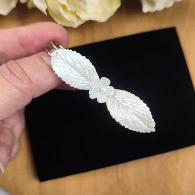 Broche attache-raîne pour robe de mariée avec deux feuilles en porcelaine froide teintes en ivoire perlé et une petite fleur acrylique au milieu