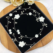 Charger l'image dans la galerie, Longue vigne de cheveux disposée en cercle sur fond noir avec fleurs en porcelaine blanche et perles nacrées sur fil argenté