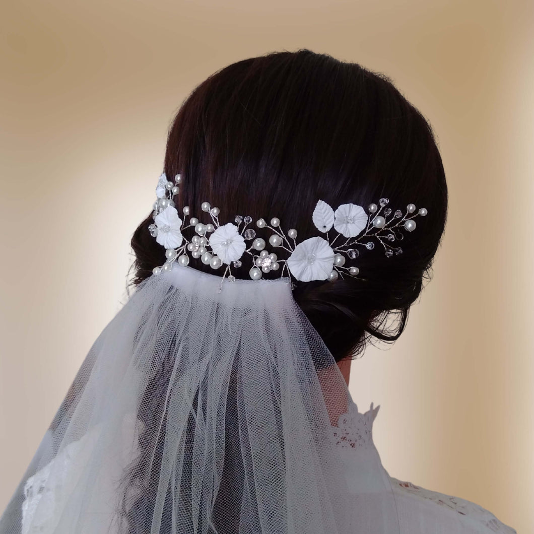 Vigne de cheveux fleurs blanches et perles pour mariage bohème ou champêtre présentée au-dessus d'un voile