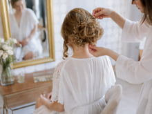 Charger l'image dans la galerie, Vigne de cheveux Amélie personnalisée avec perles dorées et cristal en cours de pose sur un chignon de mariée