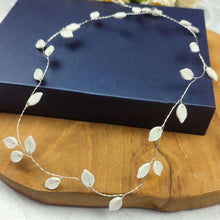 Charger l'image dans la galerie, Vigne de cheveux Flora en feuilles de porcelaine blanche présentée sur fond bleu, bijou de cheveux raffiné pour mariage.