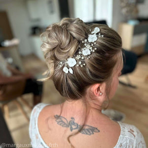 bijou de cheveux en guise de vigne de perles nacrées en verre, cristaux transparents et feuilles et fleurs blanches en porcelaine froide sur chignon haut de mariage