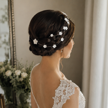 Charger l'image dans la galerie, Mariée vue de dos avec une tresse brune enroulée autour de la tête, ornée d’une vigne de cheveux fine avec fleurs blanches en porcelaine froide.