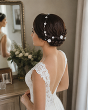 Charger l'image dans la galerie, Mariée vue de dos avec une longue vigne de fleurs blanches disposée autour d’une couronne tressée basse, sur une coiffure romantique.