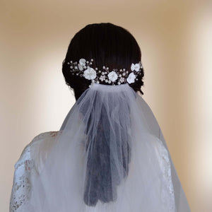 Vigne de cheveux fleurs blanches et perles pour mariage bohème ou champêtre présentée au-dessus d'un voile